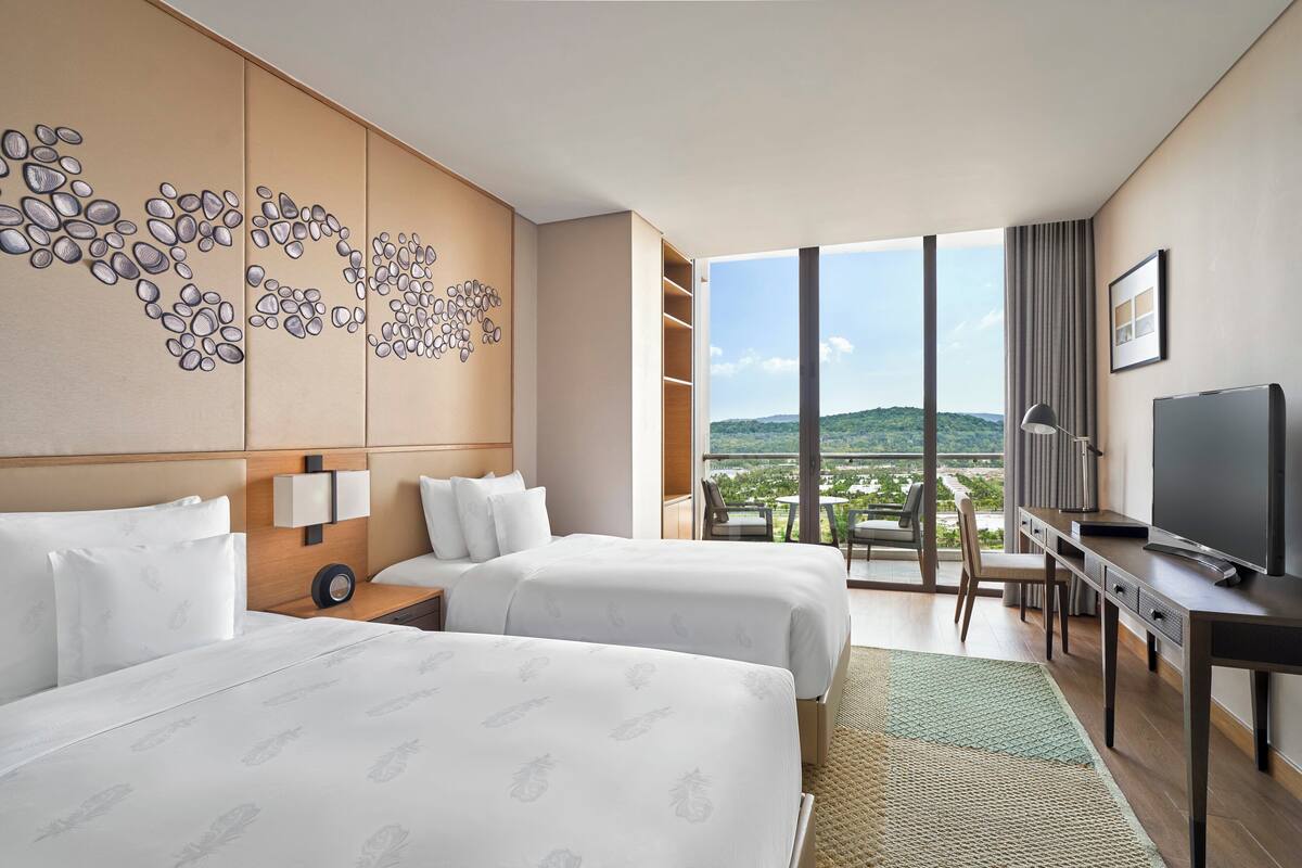 Une chambre d’hôtel avec deux lits, un bureau, une télévision et une grande fenêtre donnant sur les montagnes.