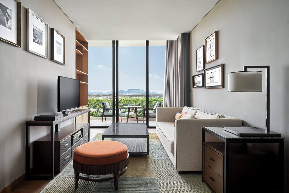 Une chambre d’hôtel moderne dotée d’une grande fenêtre, d’un téléviseur à écran plat, d’un canapé, d’une table basse et d’un bureau.