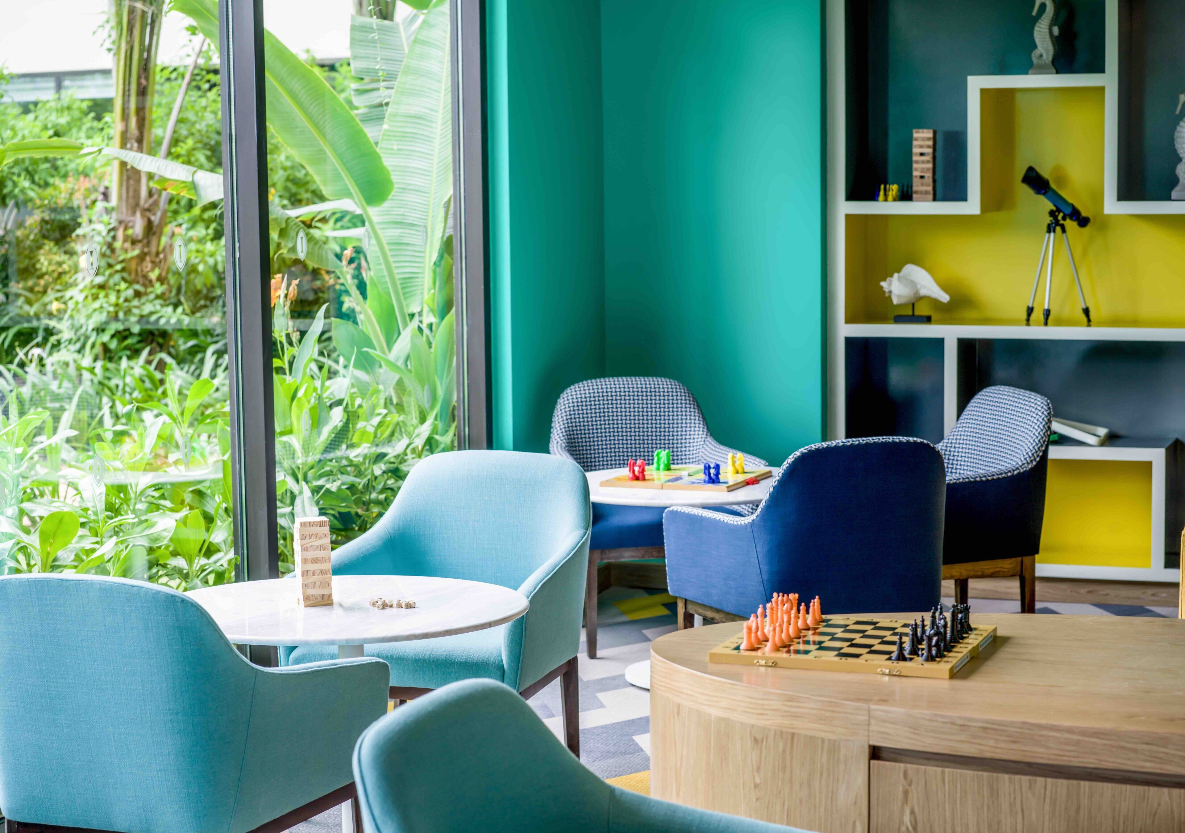 A room with two blue chairs, a small round table, and a chessboard.