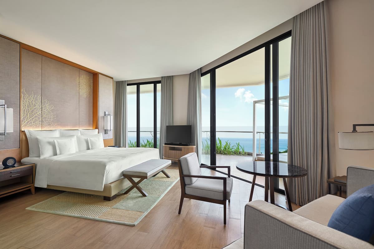 Une chambre d’hôtel moderne dotée d’un grand lit, d’une télévision, d’un balcon avec vue sur l’océan et d’un coin repas.