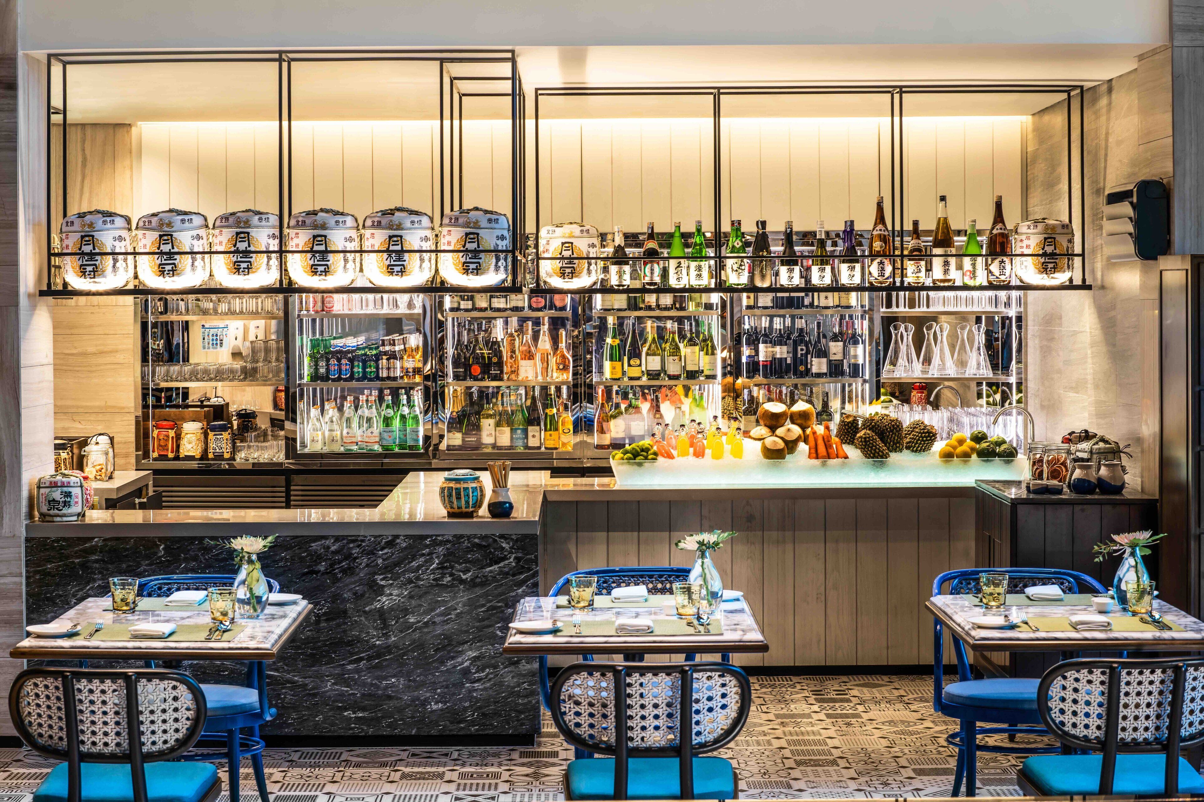 A bar area with multiple shelves of bottles and glasses, a counter with a variety of drinks, and two tables with chairs set up for dining.
