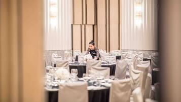 A banquet hall with tables set for a formal event, a person arranging the table settings, and a modern interior design.