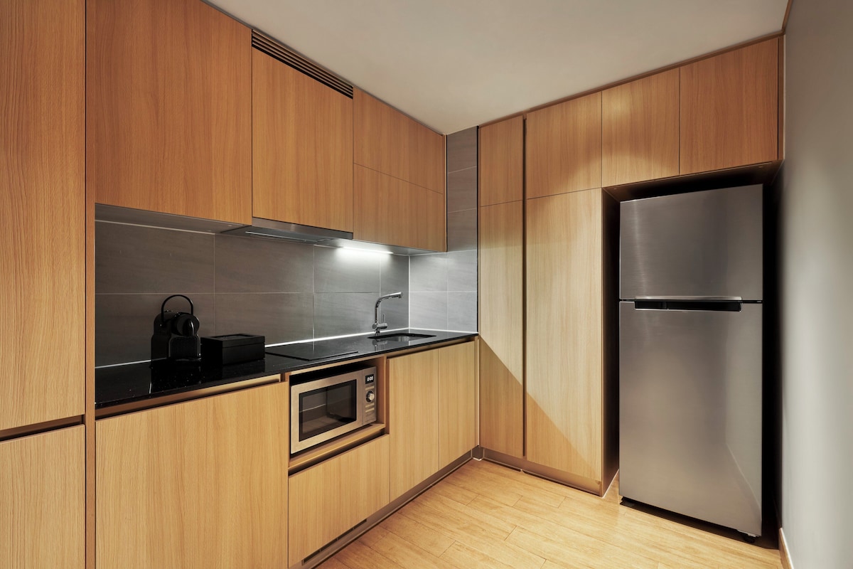 Una cocina moderna con armarios de madera, un refrigerador de acero inoxidable, un microondas y una encimera negra.