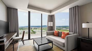 Una habitación de hotel moderna con un ventanal grande, un sofá, una mesa de centro, un televisor y un escritorio.