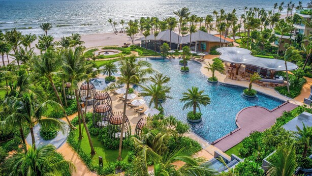 Un resort con una piscina grande, palmeras y vista a la playa.