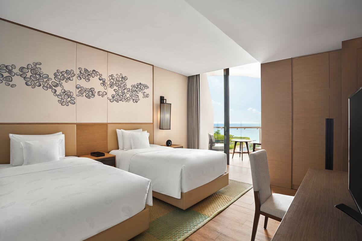A hotel room with two beds, a large window with a view, a desk, and a TV.