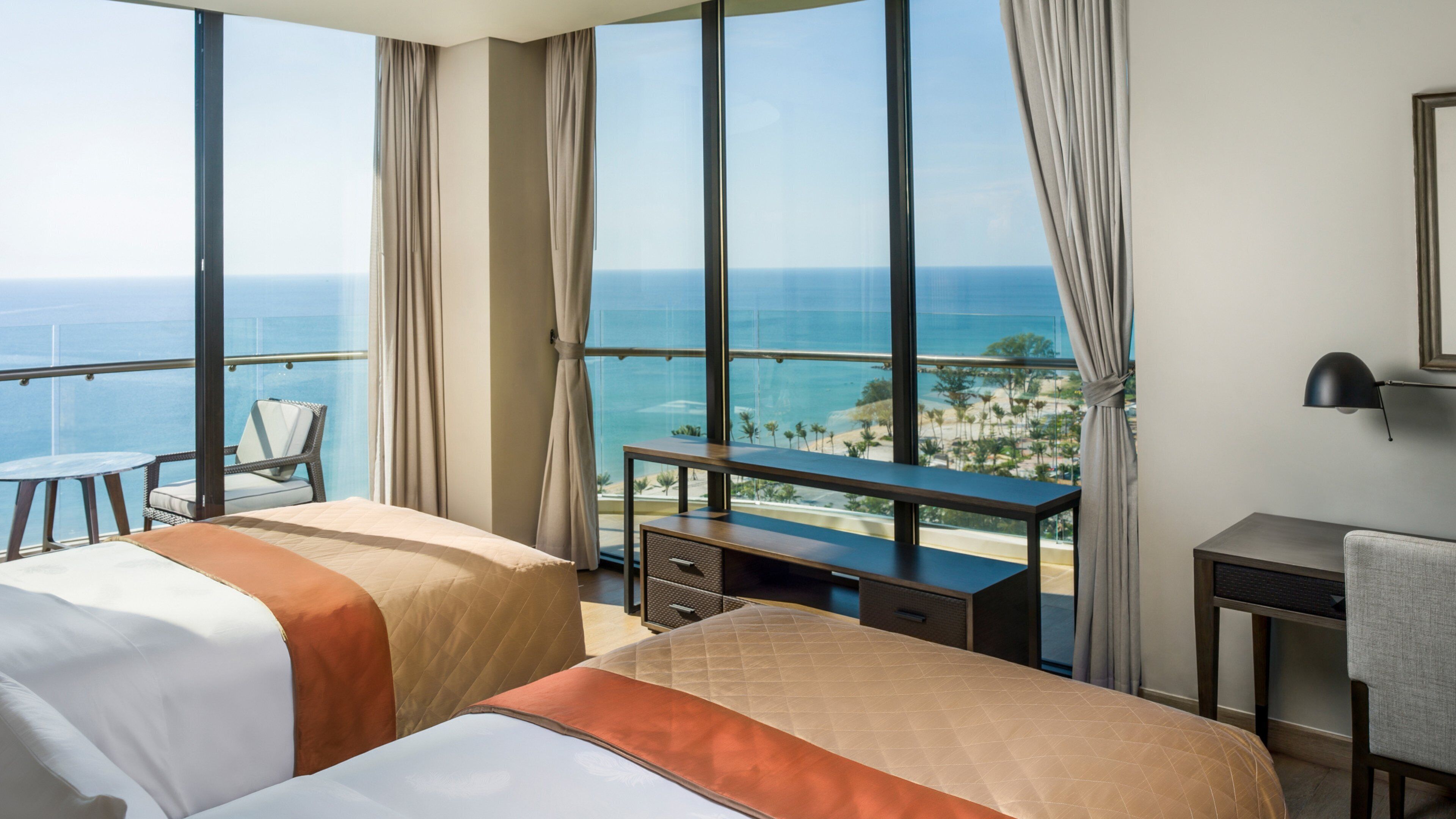 A hotel room with two beds, a desk, a chair, and a view of the ocean.