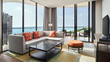 A modern hotel room with a large balcony, a sofa set, a coffee table, and a TV.