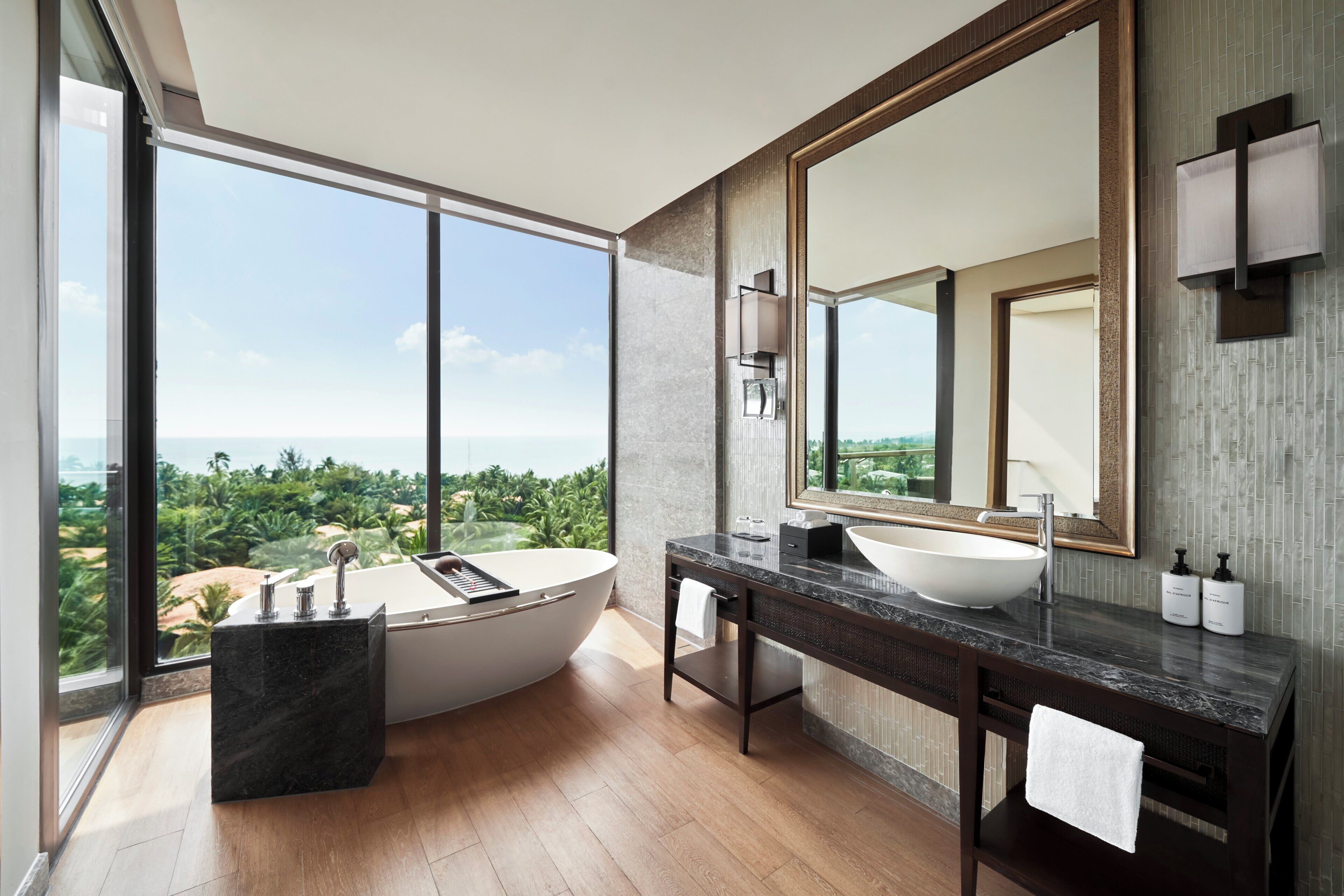 A modern bathroom with a freestanding bathtub, a large mirror, and a view of the ocean.