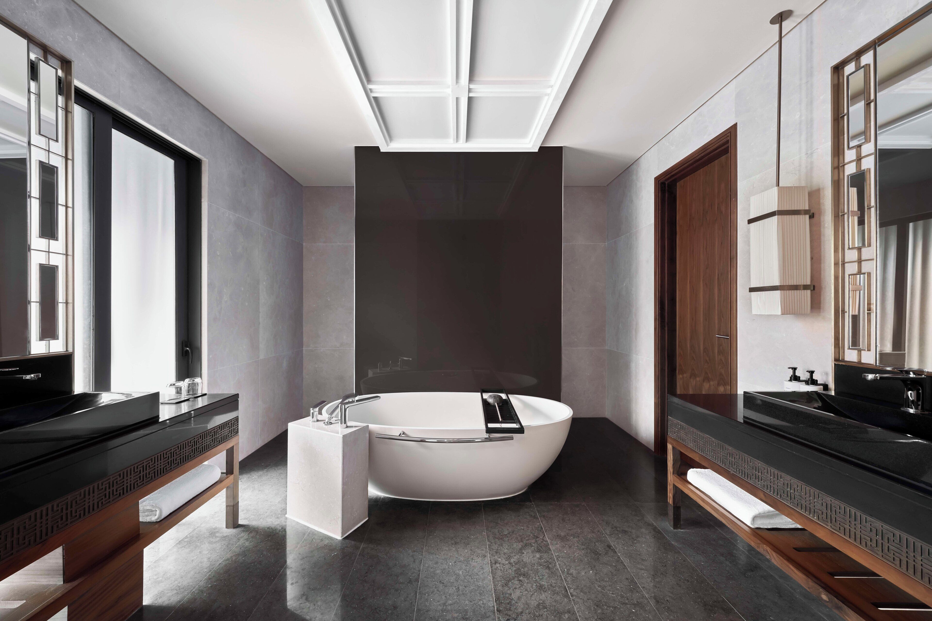 Un bagno moderno con una vasca freestanding, pavimento piastrellato scuro e elementi in legno.