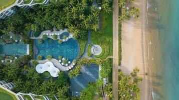 Vista aérea de un complejo turístico con piscina, palmeras y una playa.