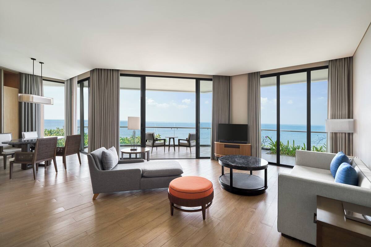 A modern hotel room with a balcony, a sofa, a dining area, and a TV.