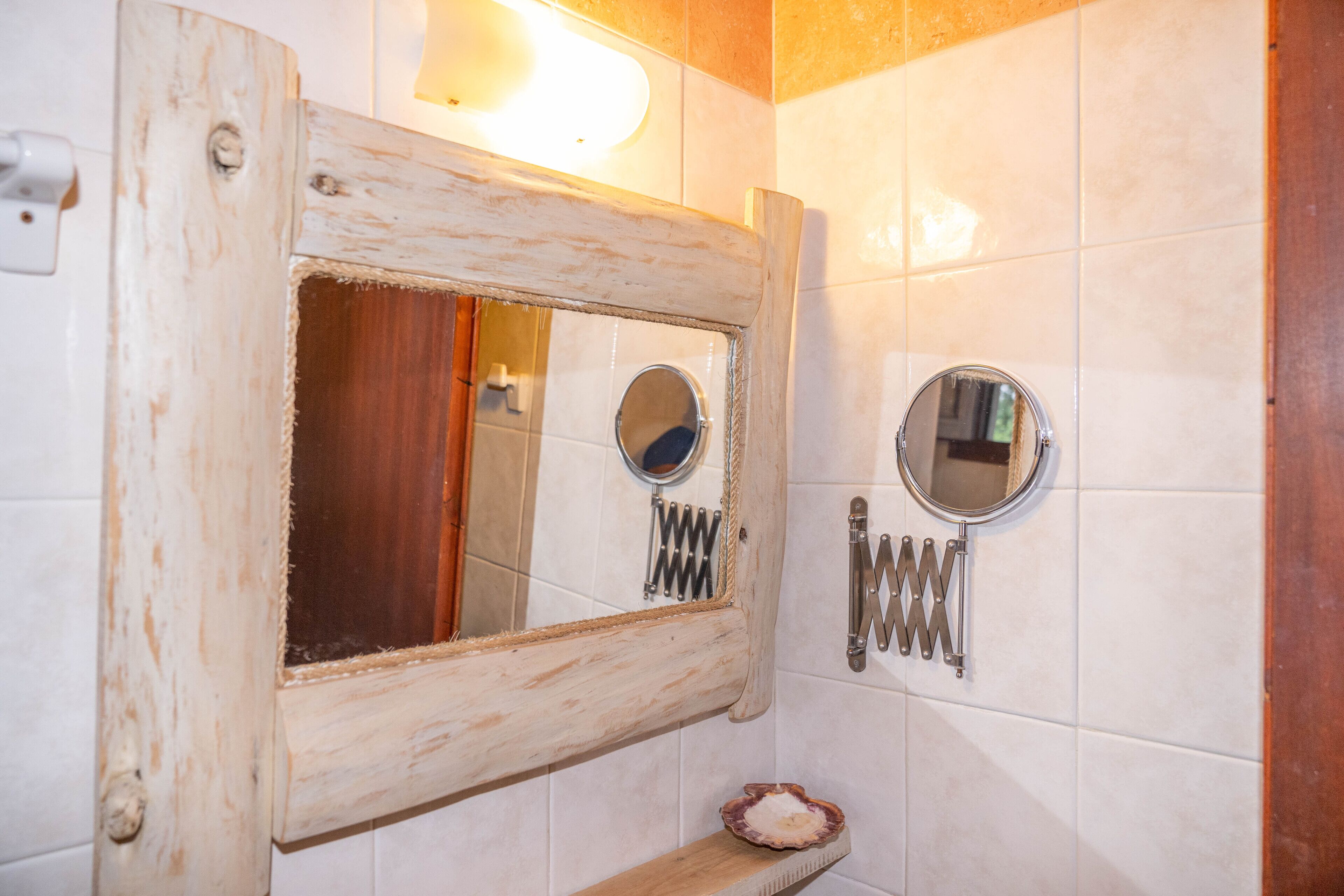 A bathroom with a rustic wooden-framed mirror, a smaller round mirror, and a towel rack with multiple towels.