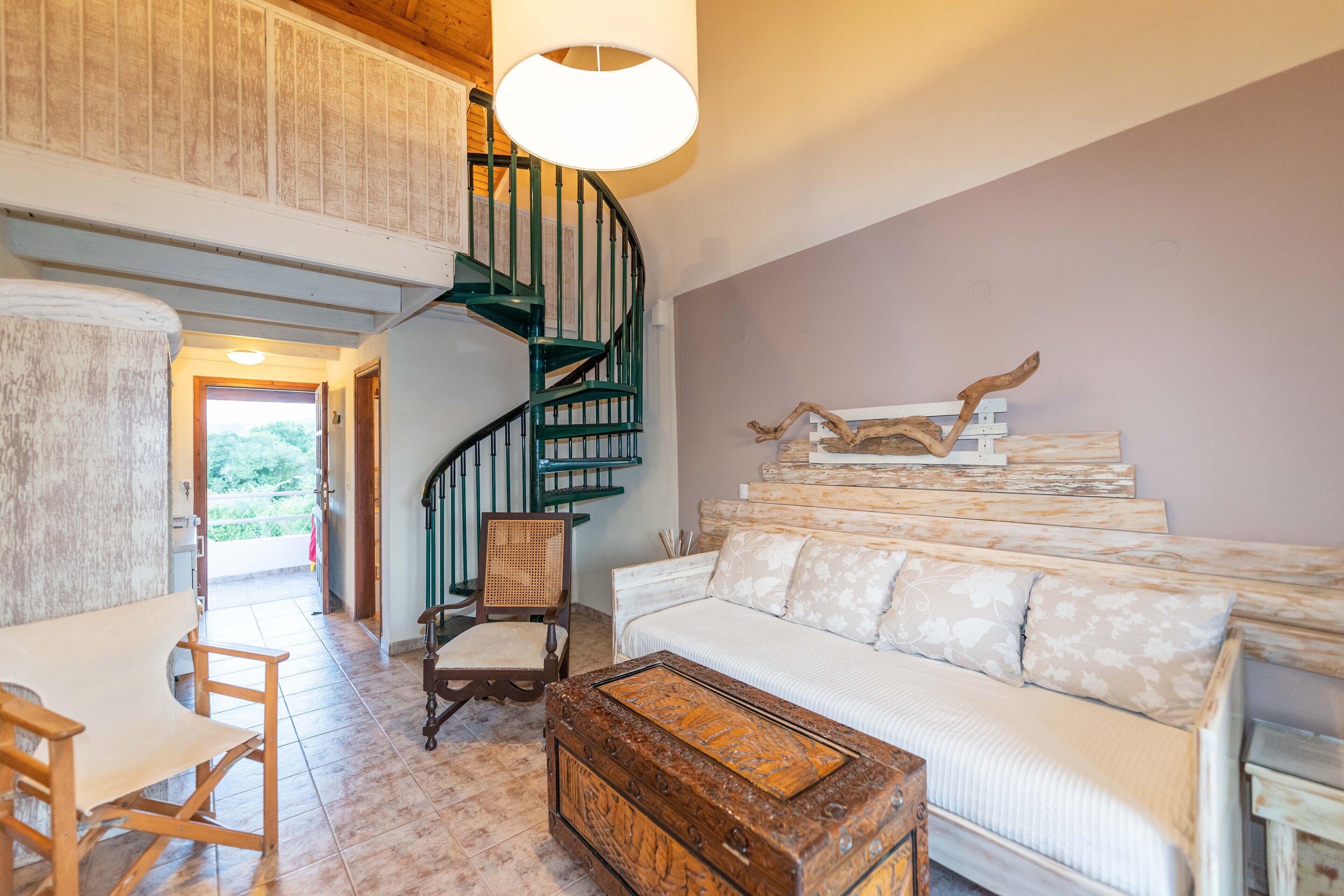 A spacious living area with a staircase, a white sofa, a wooden coffee table, and a rustic wall decor.