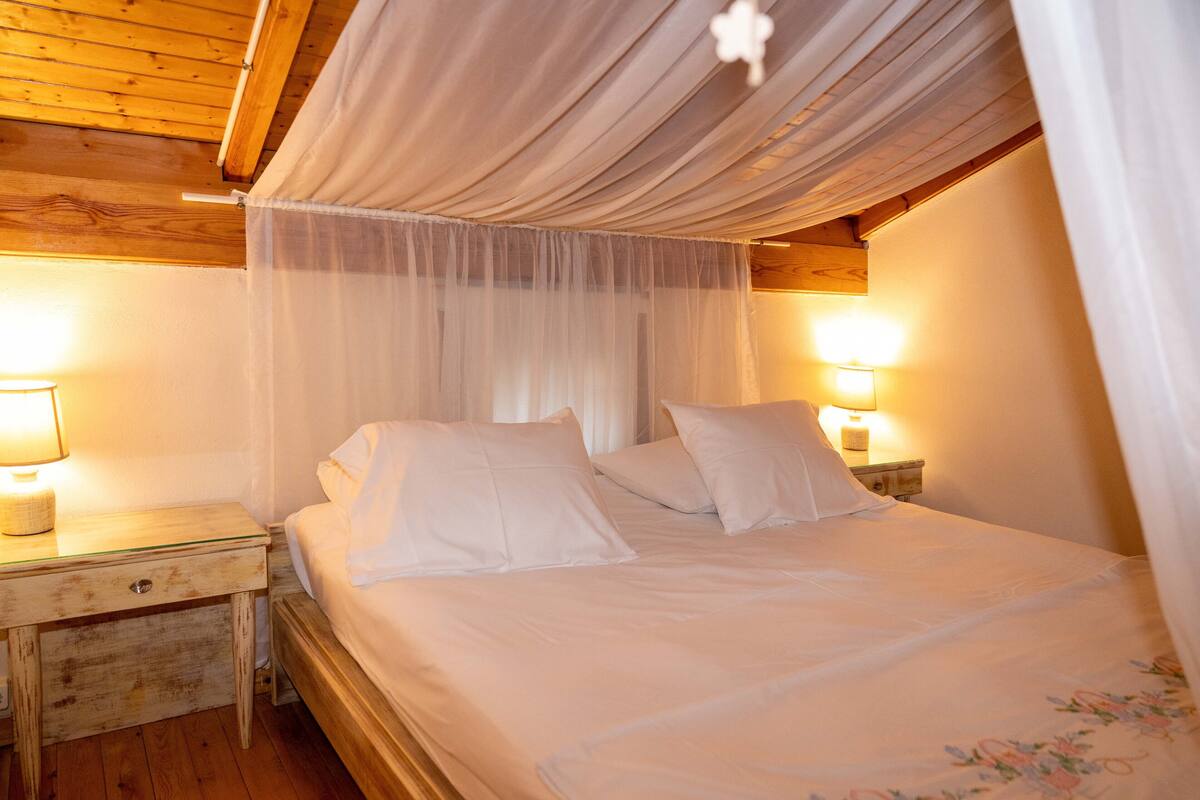 A bedroom with a canopy bed, bedside lamps, and a wooden headboard.