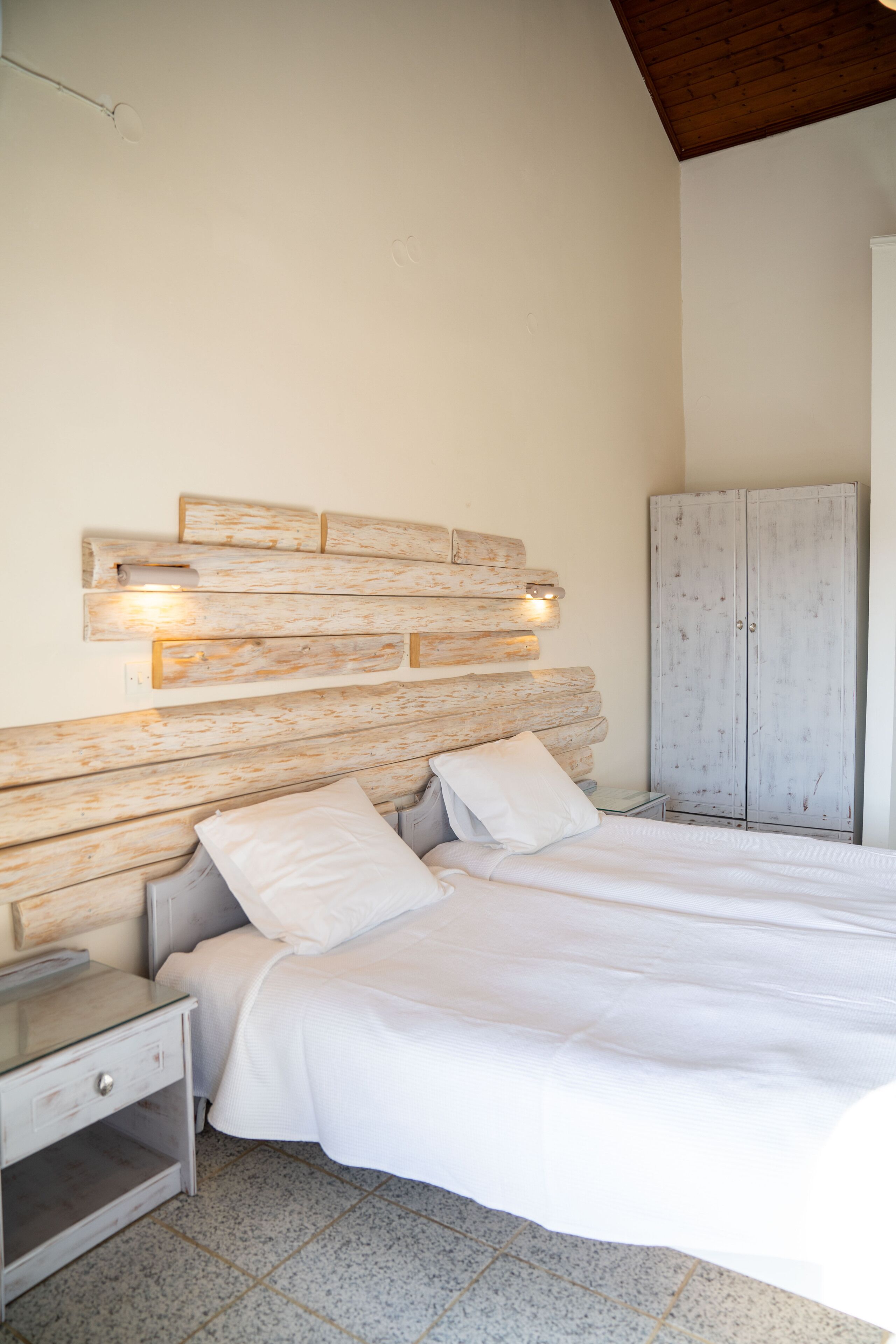 Een slaapkamer met een houten hoofdbord, een bed met witte beddengoed, een nachtkastje en een kledingkast.