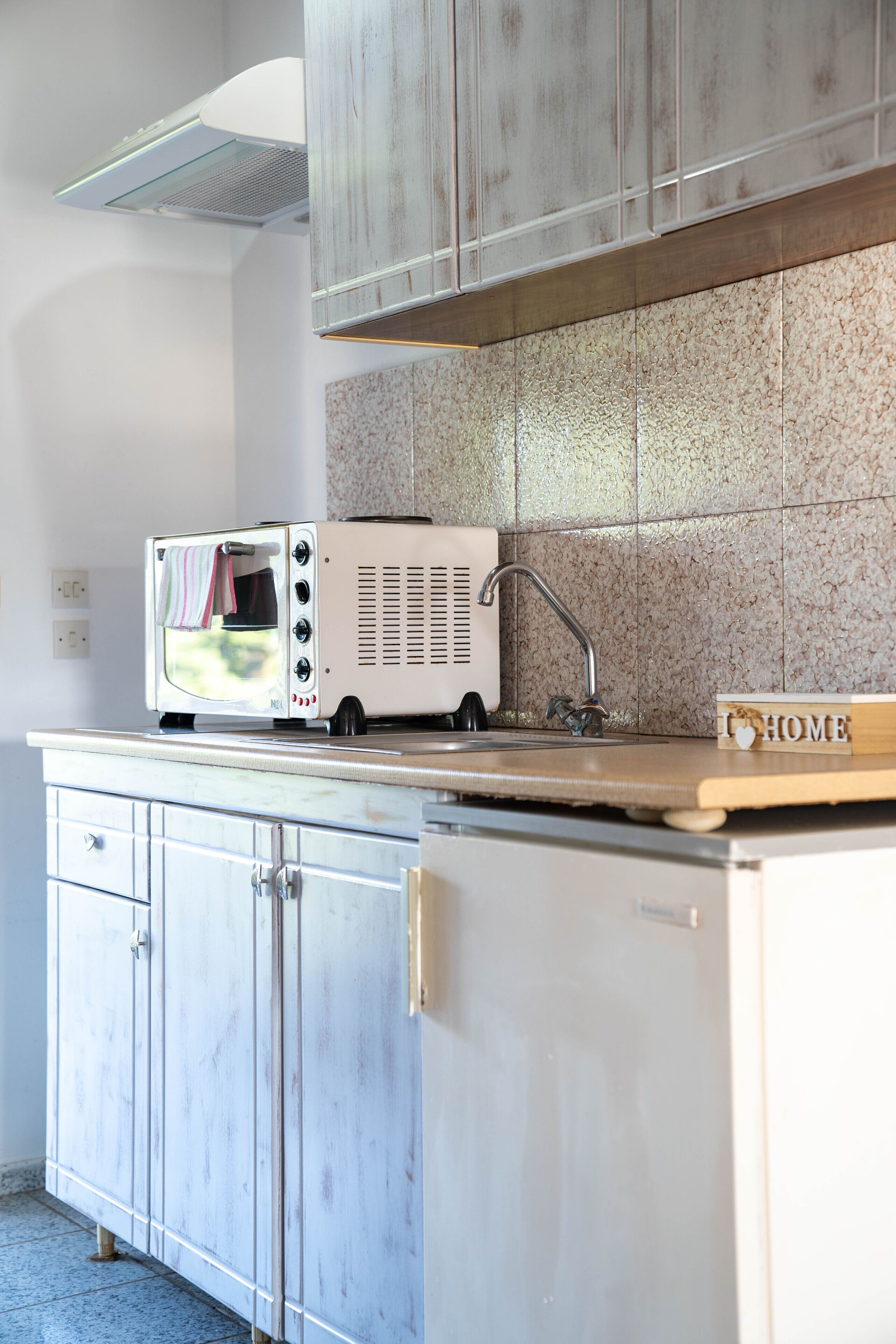 Een keuken met een vintage toaster op het aanrecht, een gootsteen en een kastje met een 'I ♥ HOME' bord.