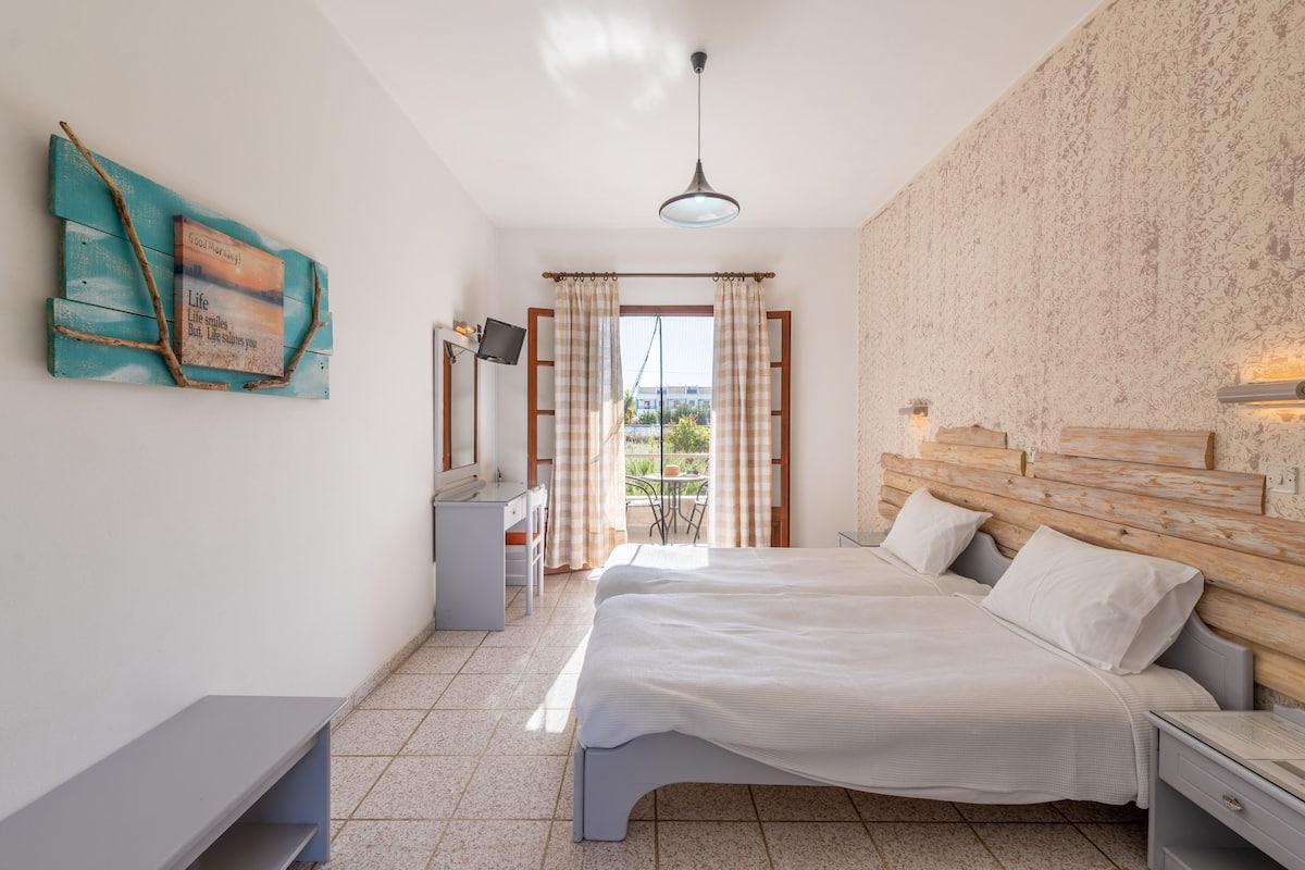 A bedroom with a bed, bedside tables, a desk, a chair, and a view through a window.