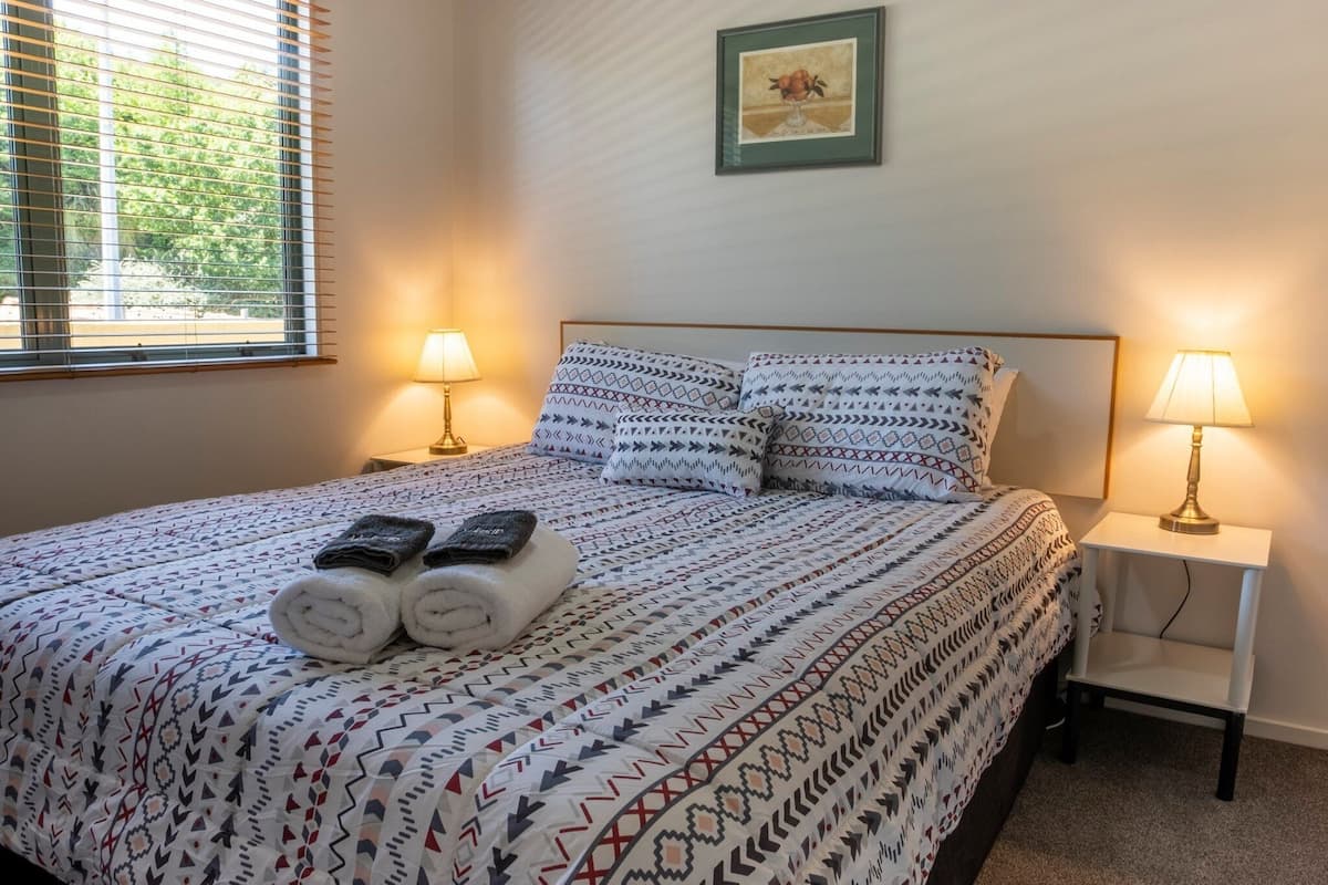 A neatly made bed with patterned bedding, two bedside lamps, and a framed picture on the wall.