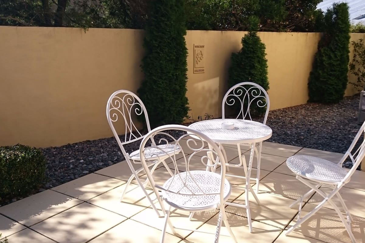 A patio with a white metal table and chairs, surrounded by a low wall and greenery.