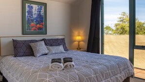 Una cama bien hecha con un edredón de lunares, dos toallas enrolladas y un cuadro floral enmarcado en la pared.
