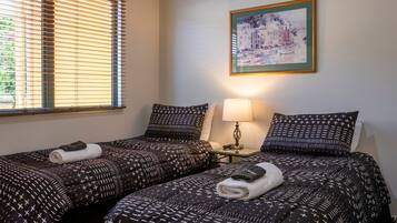 Habitación de hotel con dos camas, cada una con ropa de cama estampada y una toalla enrollada encima. Una mesita de noche con una lámpara y un cuadro en la pared.