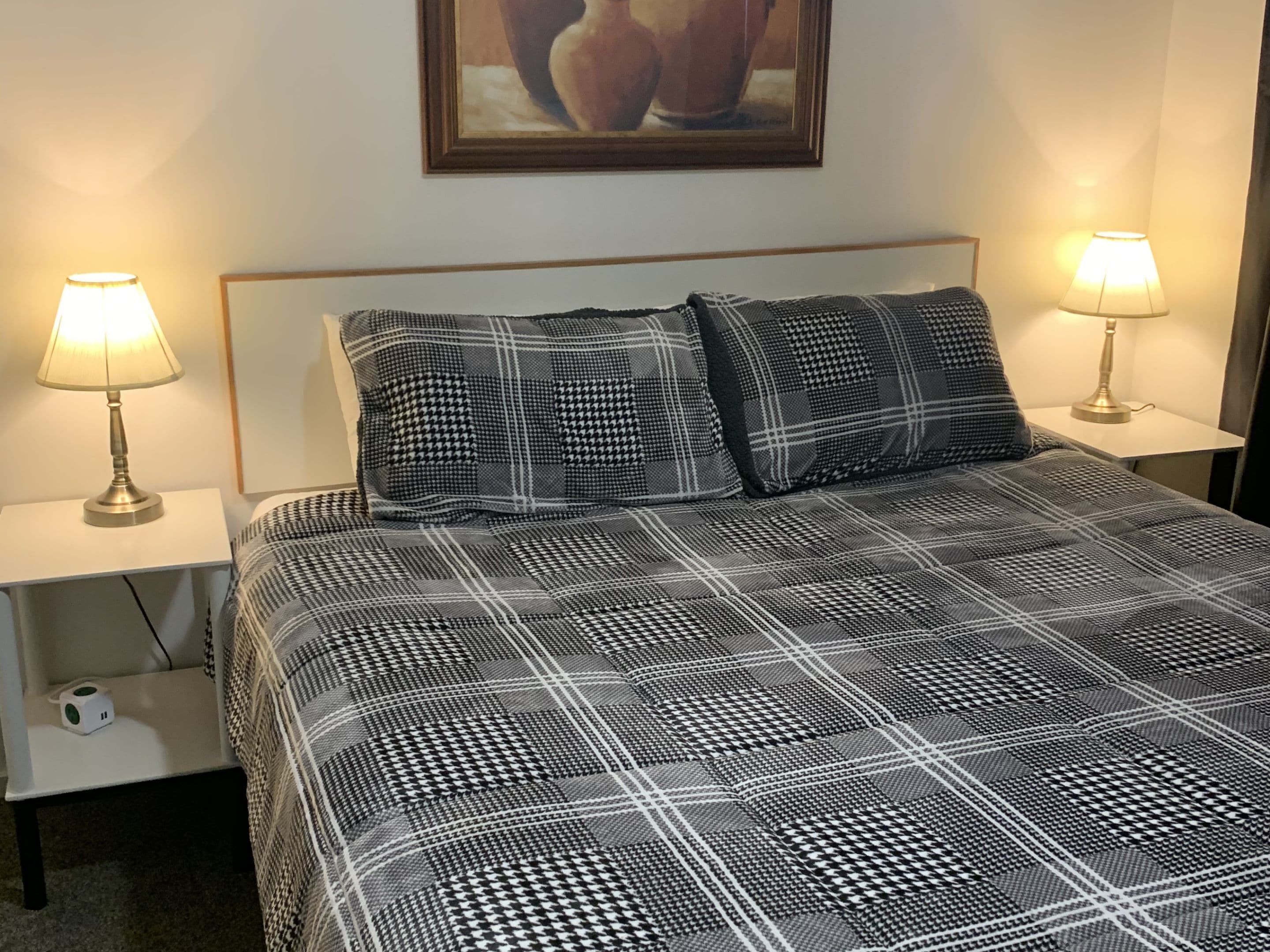 A neatly made bed with a checkered bedspread, two bedside lamps, and a framed picture on the wall.
