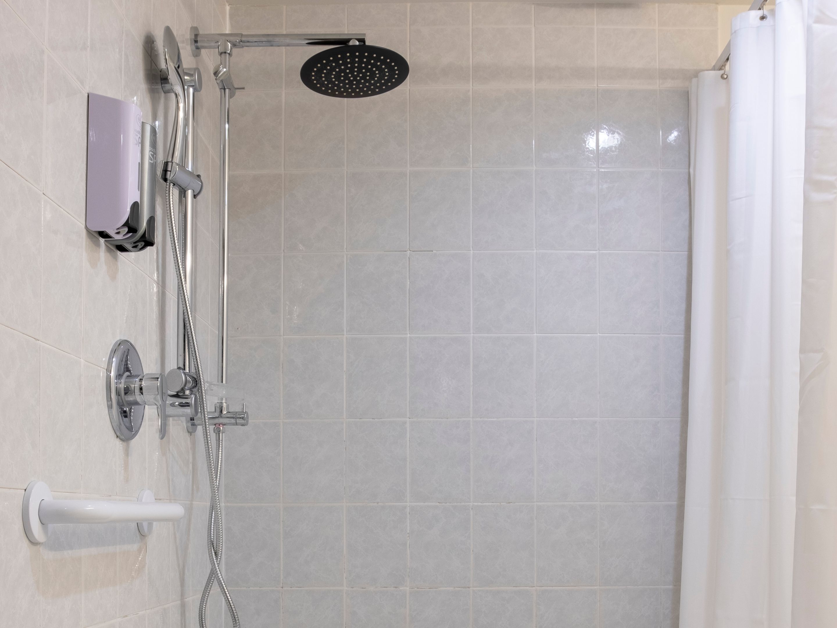 Un espace douche équipé d’un pommeau de douche à main, d’un robinet mural et d’un autre pommeau de douche à main.