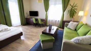 Habitación de hotel con cama, sofá verde, una mesita, televisor y planta en maceta.