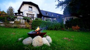 Ein Gebäude im traditionellen Baustil, mit einem Feuerkorb im Vordergrund und einem gepflegten Garten.