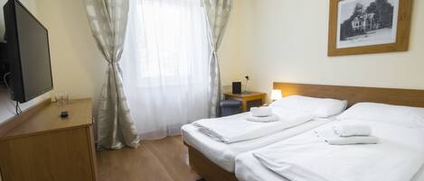 A hotel room with two beds, a desk, a TV, and a framed picture on the wall.