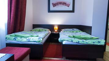 A room with two beds, a red carpet, a framed picture on the wall, and a nightstand with a lamp.