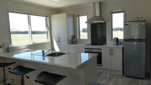 A modern kitchen with a large island, bar stools, a built-in oven, and a refrigerator. - Manuka Retreat (Ben Ohau)