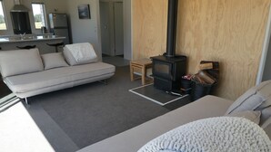 A modern living room with a sofa, a small wooden table, and a wood-burning stove. - Manuka Retreat (Ben Ohau)