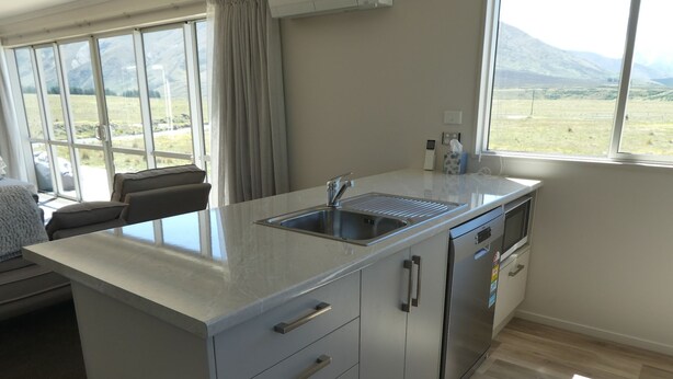 A modern kitchen with a large island, built-in appliances, and a view of a mountainous landscape. - Manuka Retreat (Ben Ohau)