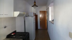 A narrow kitchen with a gas stove, a refrigerator, and a microwave. - Como en casa (Rosario)