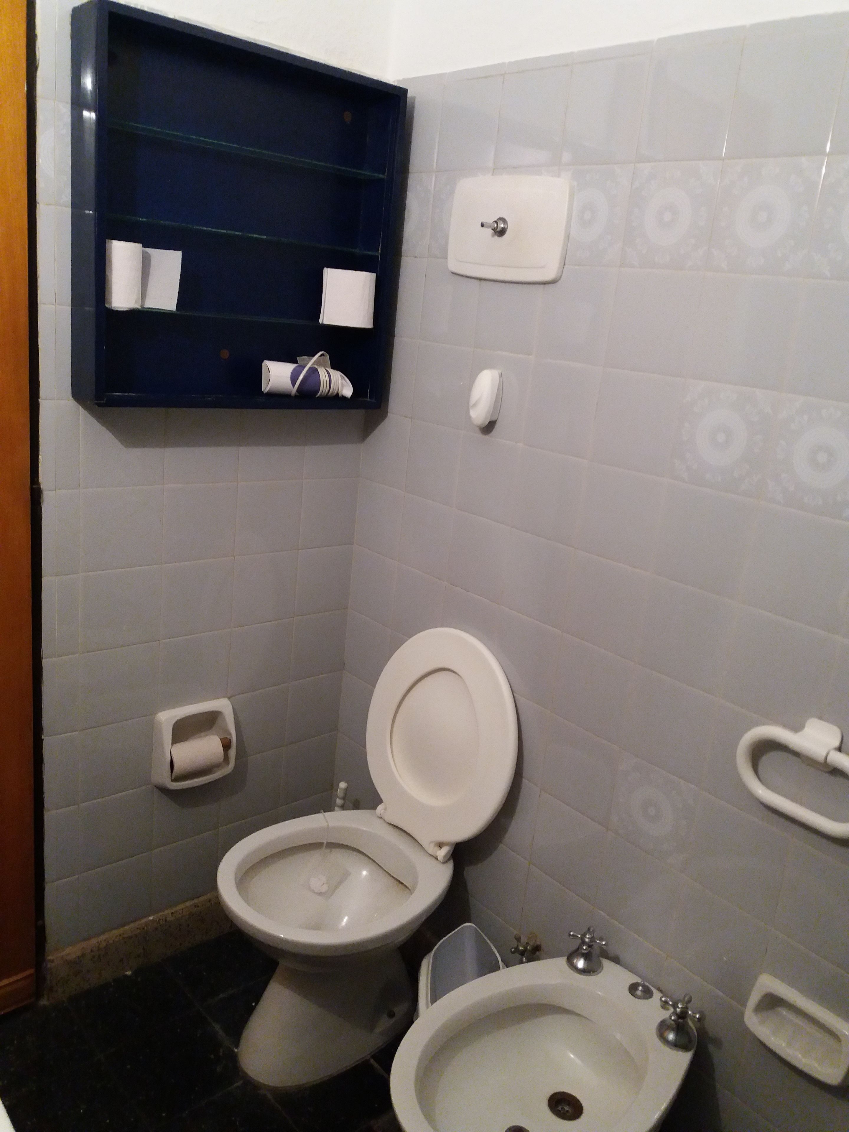 Un baño con inodoro, bidé y un estante azul con toallas y papel higiénico.