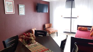 A room with a dining table, chairs, a TV mounted on the wall, and a window with curtains. - Como en casa (Rosario)