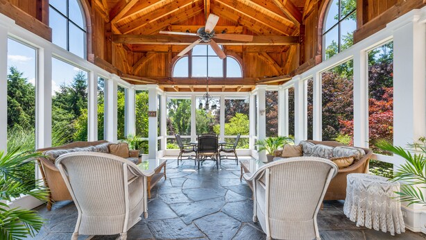 A covered patio with stone flooring, wicker furniture, and a ceiling fan.