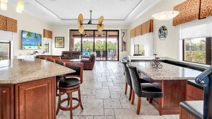 A spacious kitchen with granite countertops, wooden cabinets, and a large island with bar stools. - Reunion Paradise | 5BR Modern Oasis w/ Infinity Pool, Themed Rooms, and Game Rooms Near Disney (Kissimmee)