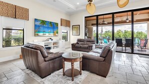 A spacious living room with leather sofas, a glass coffee table, and a large window overlooking a balcony. - Reunion Paradise | 5BR Modern Oasis w/ Infinity Pool, Themed Rooms, and Game Rooms Near Disney (Kissimmee)