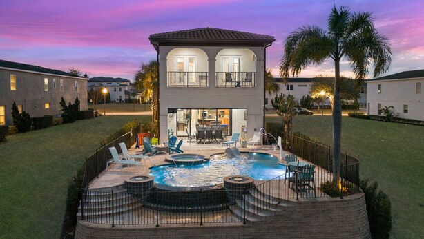 A two-story house with a backyard pool, outdoor seating, and a well-lit entrance. - Reunion Paradise | 5BR Modern Oasis w/ Infinity Pool, Themed Rooms, and Game Rooms Near Disney (Kissimmee)