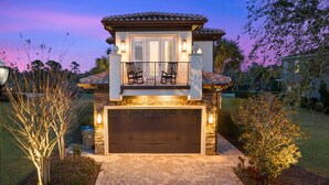 A two-story house with a garage, a balcony with chairs, and a stone facade. - Reunion Paradise | 5BR Modern Oasis w/ Infinity Pool, Themed Rooms, and Game Rooms Near Disney (Kissimmee)