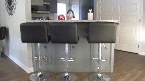 A kitchen with a central island, three bar stools, and a white door in the background. - Kathy's Kottage. Bungalow on the side of Missionary Ridge, Furry Friends Welcome (Chattanooga)
