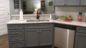 A kitchen with grey cabinets, a stainless steel dishwasher, and a granite countertop. - Kathy's Kottage. Bungalow on the side of Missionary Ridge, Furry Friends Welcome (Chattanooga)