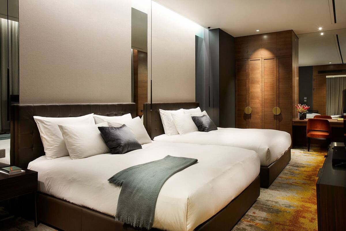 Une chambre d’hôtel moderne avec deux lits, un bureau et un miroir.