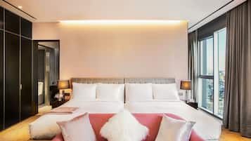 A modern hotel room with a large bed, a red sofa, and a view of the city through the window.