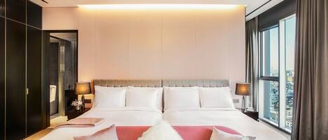 A modern hotel room with a large bed, a red sofa, and a view of the city through the window.