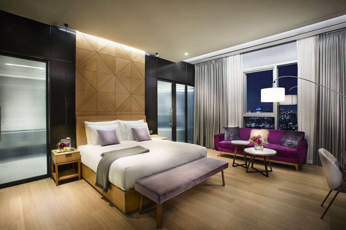 Une chambre d’hôtel moderne avec un grand lit, un canapé, une table basse et une vue sur la ville par la fenêtre.