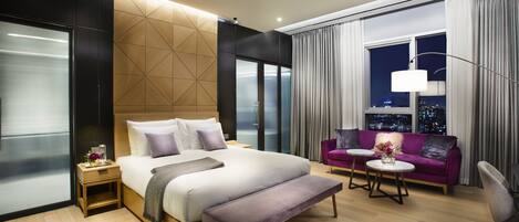 Habitación de hotel moderna con una cama grande, un sofá, una mesa de centro y vistas a la ciudad desde la ventana.